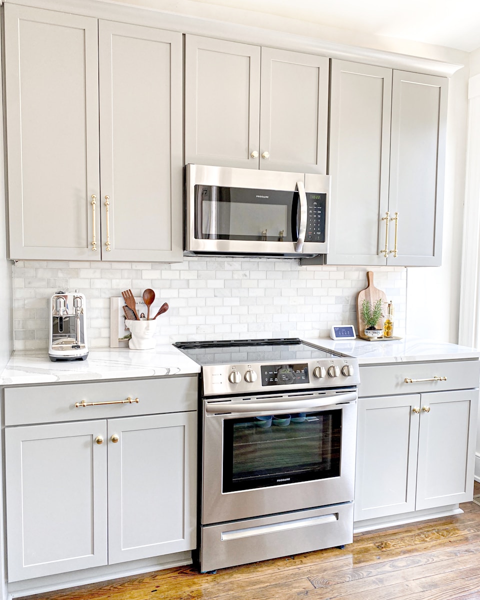 Gray kitchen cabinets with stone counters and brass hardware